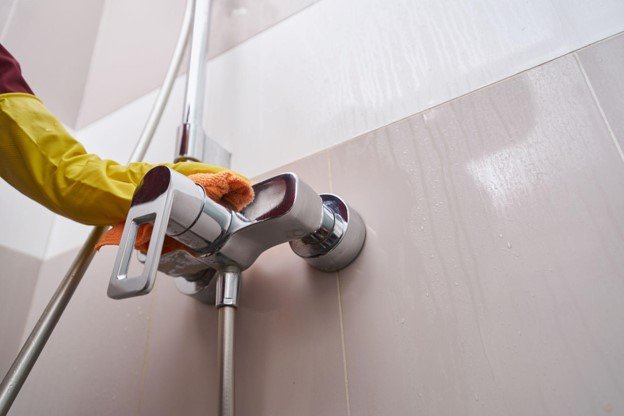 Bathroom professional inspecting and cleaning a chrome shower fixture after installation.