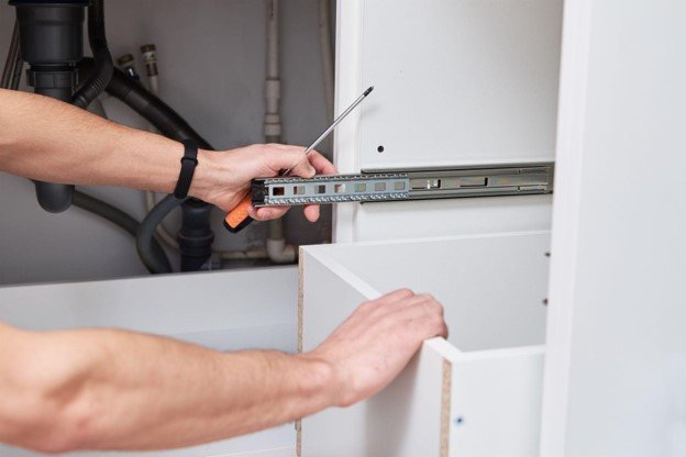 Professional installer fitting a drawer slide inside a bathroom cabinet during cabinet installation.