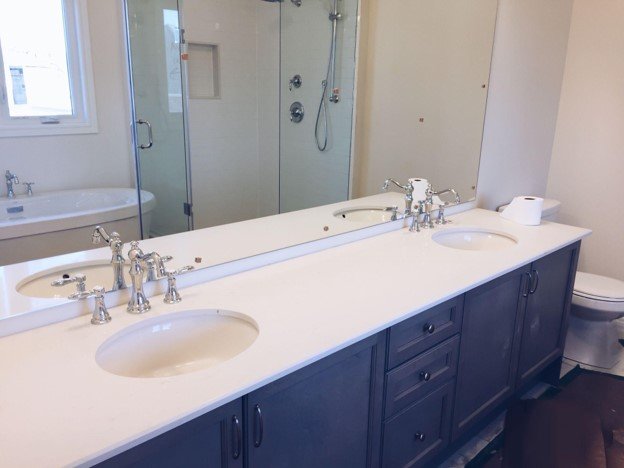 Finished double-sink bathroom countertop installed over vanity cabinets with faucets and large mirror
