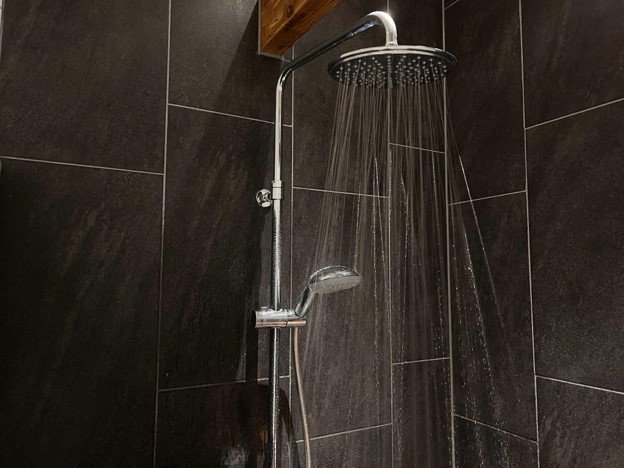 Finished shower surround with dark wall tile, rainfall showerhead, and handheld shower fixture.