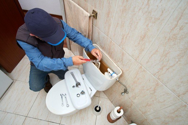 Bathroom professional repairing and adjusting toilet tank components during a toilet installation
