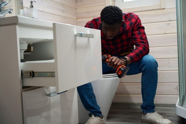 Bathroom installer using a power drill while fitting a vanity cabinet in a residential bathroom