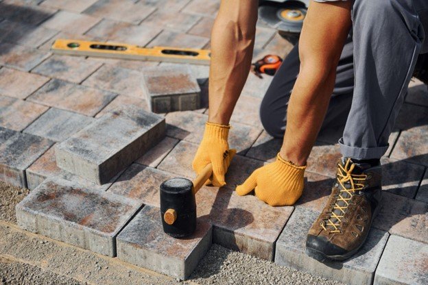 Professional installer setting and leveling concrete pavers with a rubber mallet during patio installation in Forney, TX
