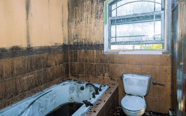 Old and outdated bathroom with damaged surfaces, bathtub, toilet, and wall tile before remodeling.
