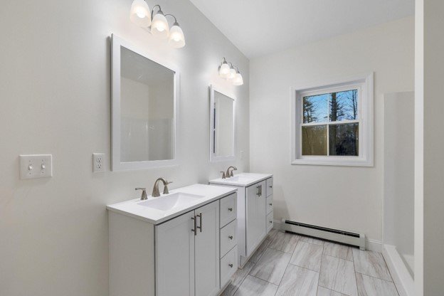 Completed bathroom vanity installation with dual white vanities, sinks, mirrors, lighting, and tile flooring.