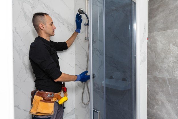Contractor installing a glass shower surround and shower fixtures in a remodeled bathroom.